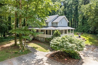Farmhouse-style home featuring a porch, a shingled roof, concrete driveway, and a forest view