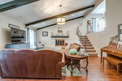 Living room with brick wall, wood finished floors, a fireplace, and stairway