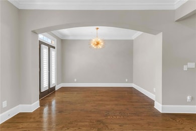Unfurnished room with arched walkways, a chandelier, ornamental molding, baseboards, and wood finished floors