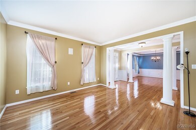 Unfurnished room with ornate columns, light wood-type flooring, plenty of natural light, ornamental molding, and a chandelier