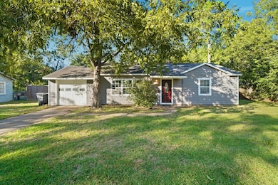 Charming single-story home with neutral exterior, nestled among mature trees. It features a one-car garage, a welcoming front door, and a well-maintained lawn.