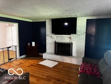 living room featuring a textured ceiling, wood finished floors, a fireplace, and crown molding