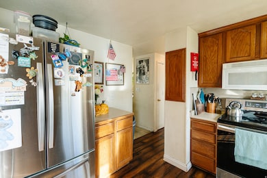 Kitchen with appliances with stainless steel finishes, light countertops, brown cabinetry, and dark wood-type flooring