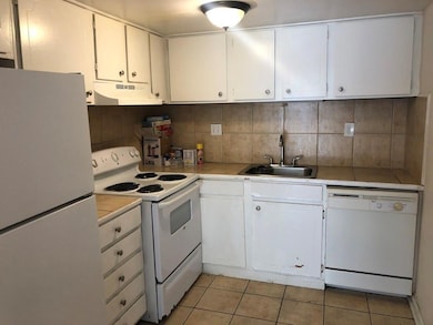 Kitchen featuring white appliances, under cabinet range hood, a sink, and light tile patterned floors