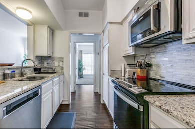 Kitchen with appliances with stainless steel finishes, backsplash, light stone counters, white cabinets, and dark wood-style floors