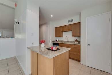 Kitchen with light tile patterned floors, light stone counters, recessed lighting, a peninsula, and brown cabinetry