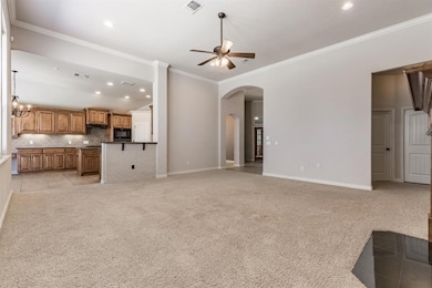 Unfurnished living room featuring ceiling fan, arched walkways, light carpet, ornamental molding, and recessed lighting