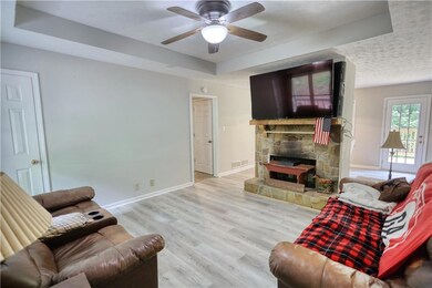 Living room featuring a raised ceiling, ceiling fan, a fireplace, and wood finished floors