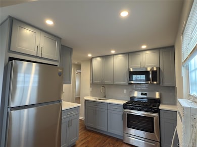 Kitchen featuring appliances with stainless steel finishes, gray cabinets, recessed lighting, dark wood-type flooring, and tasteful backsplash
