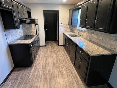 Kitchen featuring dark cabinets, black appliances, and light wood-style floors