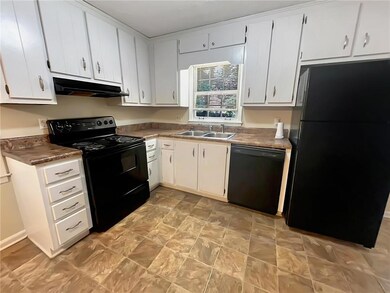 Kitchen with black appliances, under cabinet range hood, white cabinets, and dark countertops