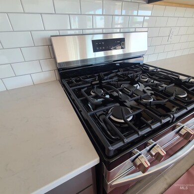 Kitchen view of stainless steel range with gas cooktop, backsplash, and light stone countertops