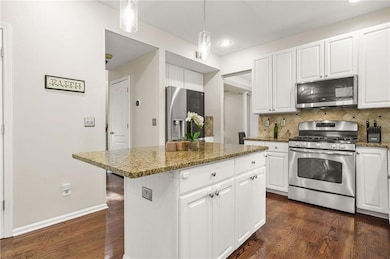Kitchen with stainless steel appliances, tasteful backsplash, dark wood-type flooring, white cabinets, and a kitchen island