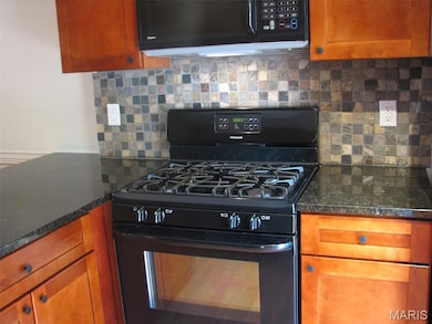Kitchen featuring black appliances, backsplash, brown cabinets, and dark stone countertops