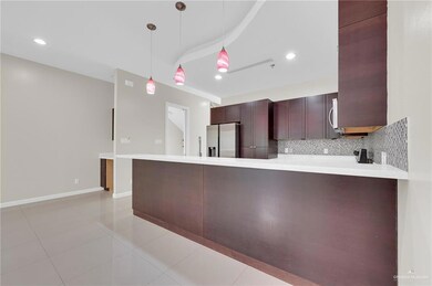 Kitchen with stainless steel fridge, a peninsula, light countertops, decorative backsplash, and decorative light fixtures