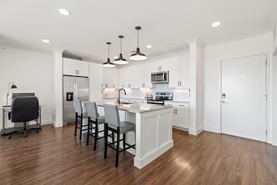 Kitchen featuring white cabinets, decorative backsplash, a center island with sink, decorative light fixtures, and light stone countertops