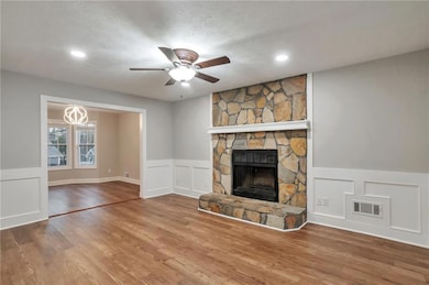 Unfurnished living room with a textured ceiling, a decorative wall, a fireplace, ceiling fan, and a wainscoted wall