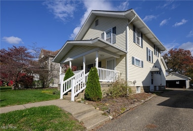 View of front of home with covered porch, a detached garage, an outbuilding, and a front lawn