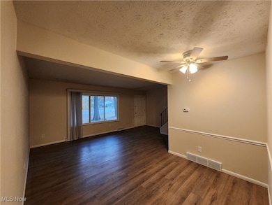 Empty room with dark wood-style flooring, a ceiling fan, a textured ceiling, and stairs
