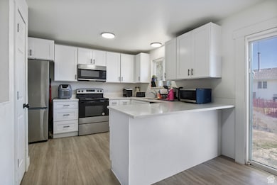 Kitchen with light wood-type flooring, white cabinetry, stainless steel appliances, and a peninsula
