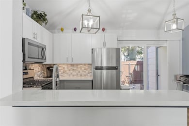 Kitchen featuring backsplash, appliances with stainless steel finishes, white cabinets, light stone counters, and pendant lighting