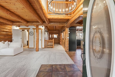Carpeted entryway with log walls, a wood ceiling with exposed beams, and a chandelier