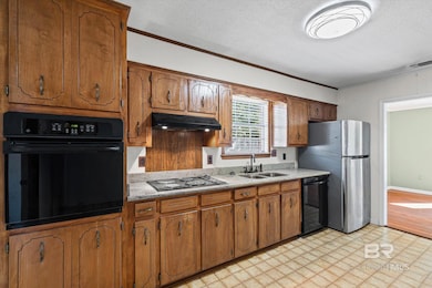 Kitchen with crown molding, a textured ceiling, black appliances, brown cabinetry, and under cabinet range hood