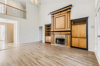 Unfurnished living room with a high ceiling, a tile fireplace, light wood finished floors, and ceiling fan