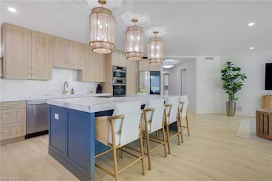 Kitchen featuring recessed lighting, light brown cabinetry, a center island, decorative light fixtures, and light wood-type flooring