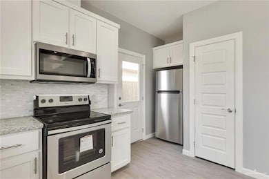 Kitchen with stainless steel appliances, white cabinetry, light wood-style flooring, light stone countertops, and backsplash