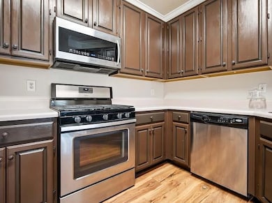 Kitchen featuring stainless steel appliances, light wood-type flooring, light countertops, and dark brown cabinetry