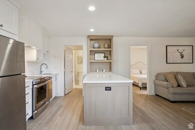 Kitchen with stainless steel appliances, white cabinets, tasteful backsplash, open shelves, and recessed lighting
