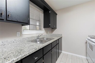Kitchen with light countertops, a sink, dark cabinetry, white range with electric stovetop, and baseboards