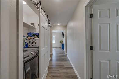 Corridor with a barn door, washer / clothes dryer, light wood-type flooring, a textured wall, and recessed lighting