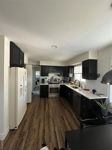 Kitchen featuring dark cabinets, refrigerator, range, dark wood-style flooring, and dishwasher