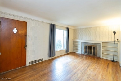 Living room featuring wallpapered walls, wood finished floors, and a fireplace & built in shelving