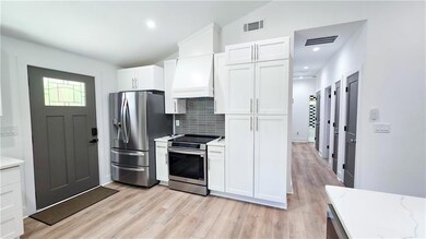 Kitchen featuring appliances with stainless steel finishes, backsplash, light wood-style floors, white cabinetry, and lofted ceiling