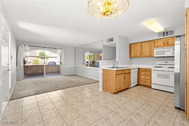 Kitchen with white appliances, light carpet, a pen
