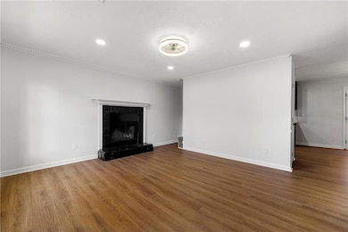 Unfurnished living room with crown molding, wood finished floors, baseboards, recessed lighting, and a premium fireplace