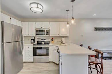 Kitchen featuring stainless steel appliances, a breakfast bar, light countertops, decorative light fixtures, and white cabinets