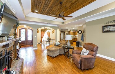 Living room with a raised ceiling, ceiling fan, light wood-type flooring, and ornamental molding