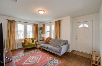 This is a cozy and well-lit living room featuring laminate floors, neutral, freshly painted walls, and large windows. Plenty of room for furniture and a simple white front door with an arched window, creating a welcoming atmosphere.