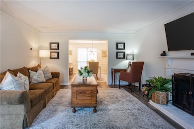 Living room with ornamental molding, wood finished floors, a chandelier, and a brick fireplace