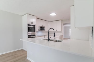 Kitchen featuring stainless steel appliances, decorative backsplash, white cabinets, light wood-style floors, and a peninsula