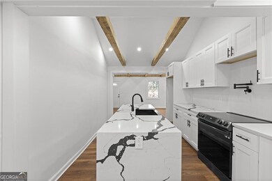 Kitchen with black range with electric cooktop, white cabinets, a center island with sink, dark wood finished floors, and recessed lighting