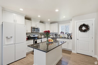 Kitchen featuring appliances with stainless steel finishes, white cabinets, dark stone countertops, recessed lighting, and light wood-style flooring
