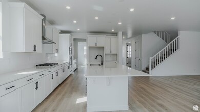 Kitchen featuring an island with sink, white cabinetry, light wood-style floors, recessed lighting, and wall chimney exhaust hood