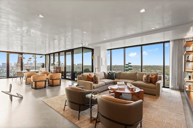 Open-plan living wrapped in floor-to-ceiling glass—soft north light by day, sunset skyline by night. Dekton floors run to a 303-sf wrap-around terrace that acts like a second living room. Segreto plaster-finished walls/ceilings + Lutron HomeWorks scene control.