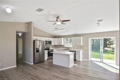 Kitchen with stainless steel appliances, white cabinets, a kitchen island, light wood finished floors, and lofted ceiling