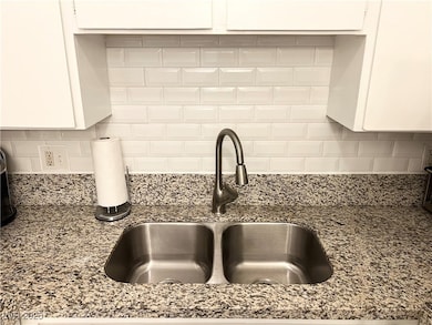 Interior details featuring tasteful backsplash, white cabinets, a sink, and stone countertops